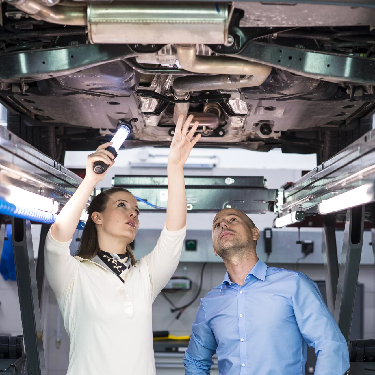 Automobil-Serviceberater:in mit eidg. Fachausweis unter dem Auto während der Beratung von Kundschaft.