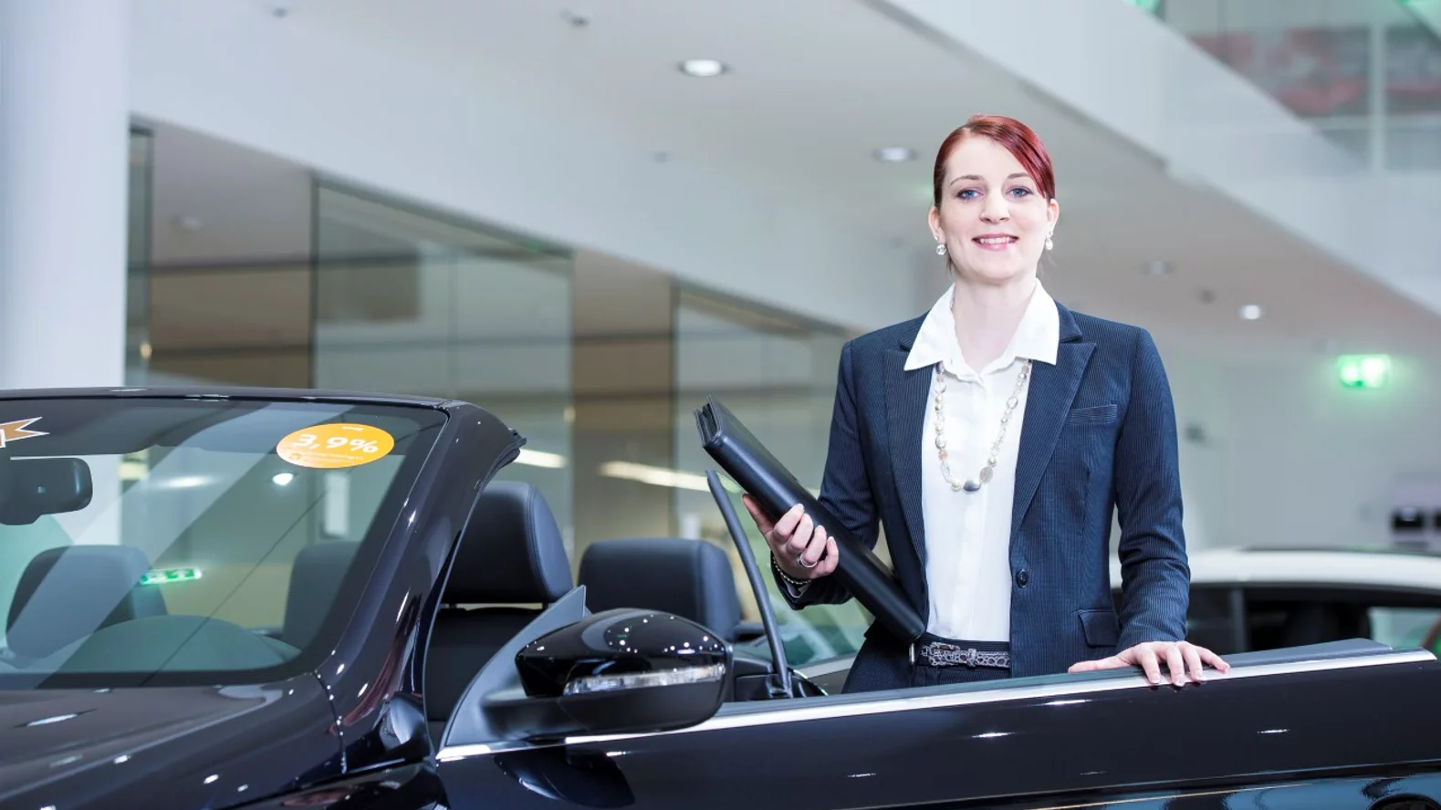 Conseiller/ère de vente d’automobiles avec brevet fédéral devant un véhicule dans le showroom.